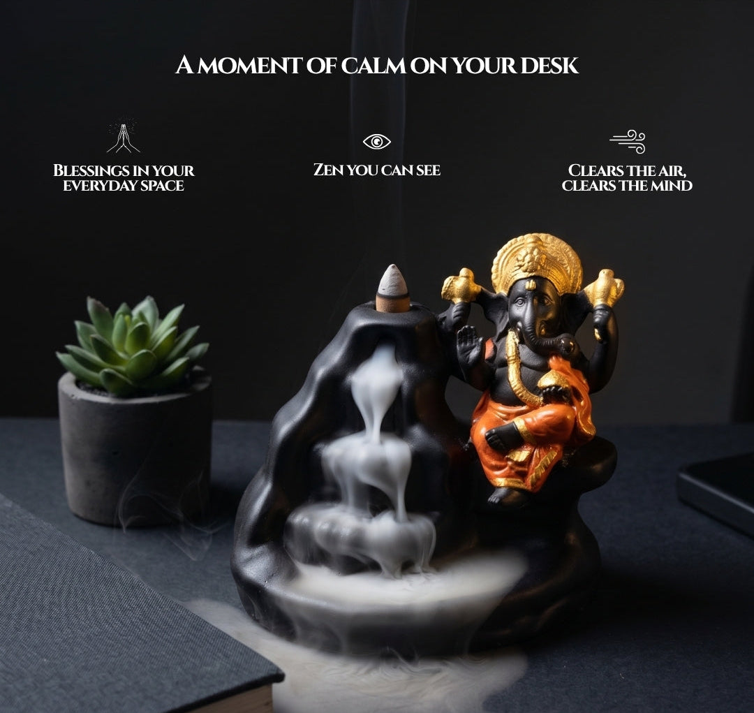 A black and gold Ganesha backflow incense burner statue with white smoke cascading down, styled on a dark desk next to a small potted succulent and a closed book, with promotional text above.